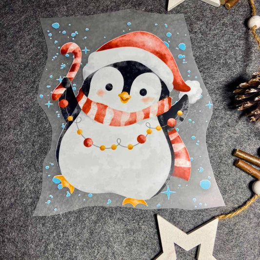 Weihnchtsbügelbild mit einem Pinguin mit Weihnachtsmütze auf und Schal um und einer Zuckerstange und Lichterkettte n der hand